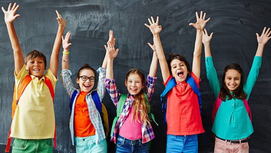 Excited schoolchildren standing with hands up